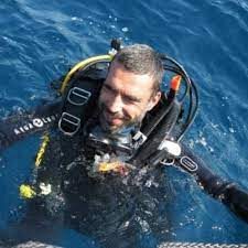 struttore subacqueo che emerge dall'acqua con un sorriso radioso, simboleggiando l'avventura e la passione per il mondo sottomarino a diving puglia d.c.